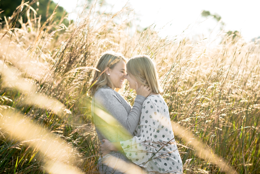 A woman pulls her girlfriend in for a kiss in the tall grass during their west chester engagement session.